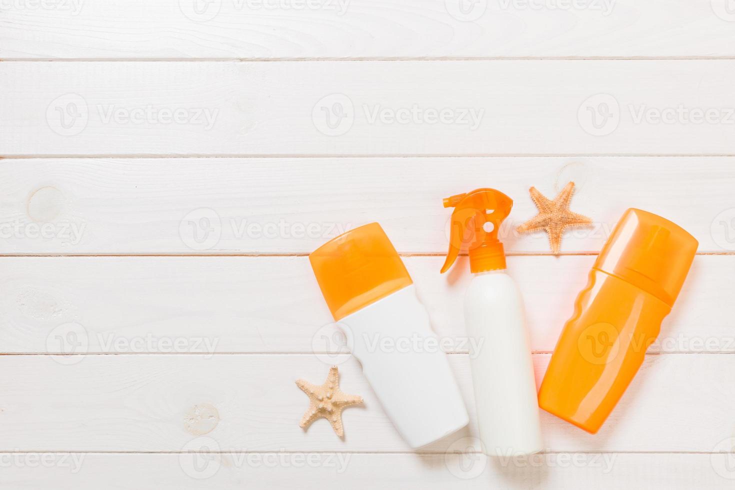 frascos de protetor solar com conchas na mesa de madeira branca. vista superior de acessórios de saúde de viagem foto
