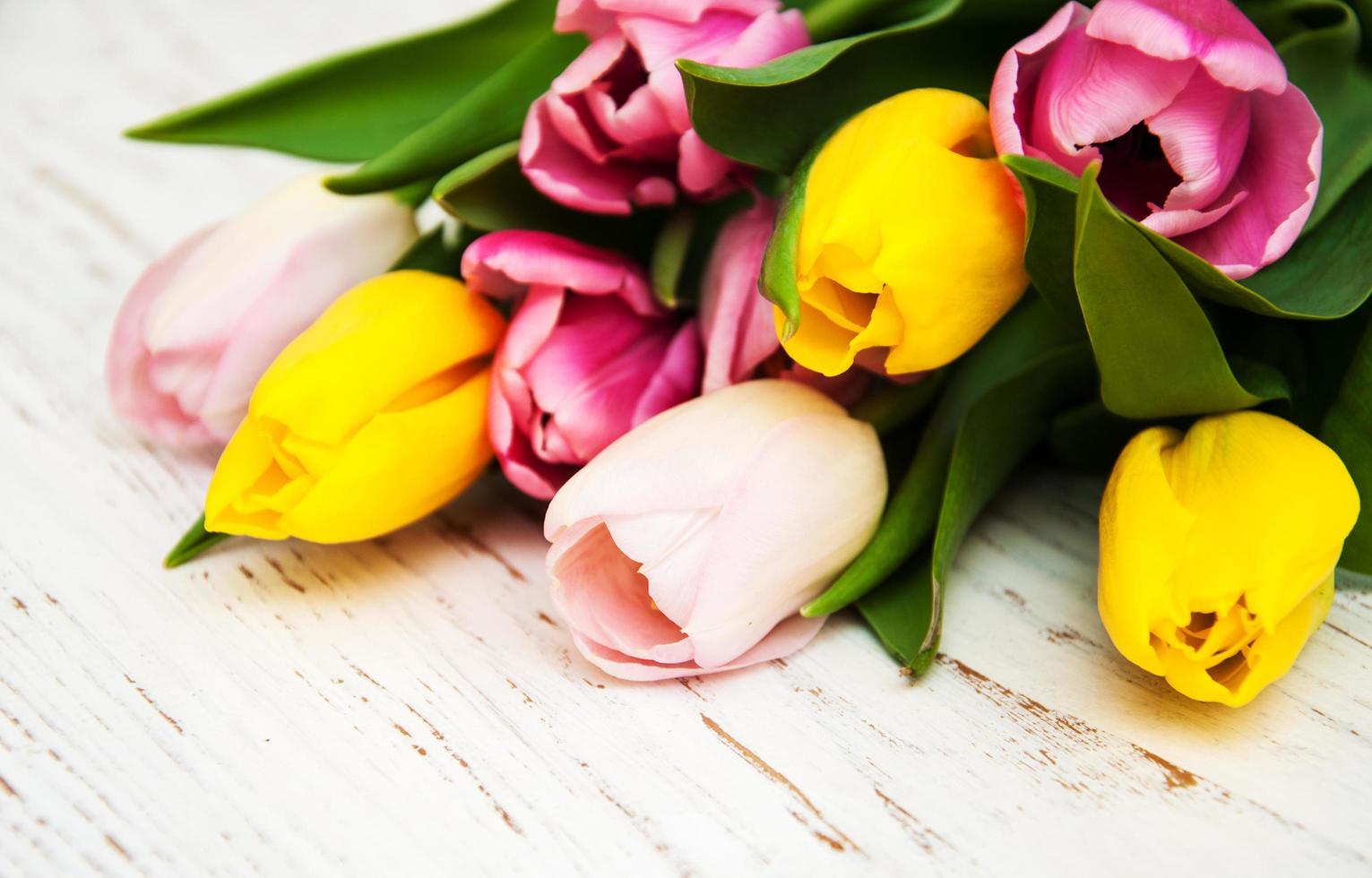 buquê de tulipas rosa e amarelas em um fundo de madeira foto