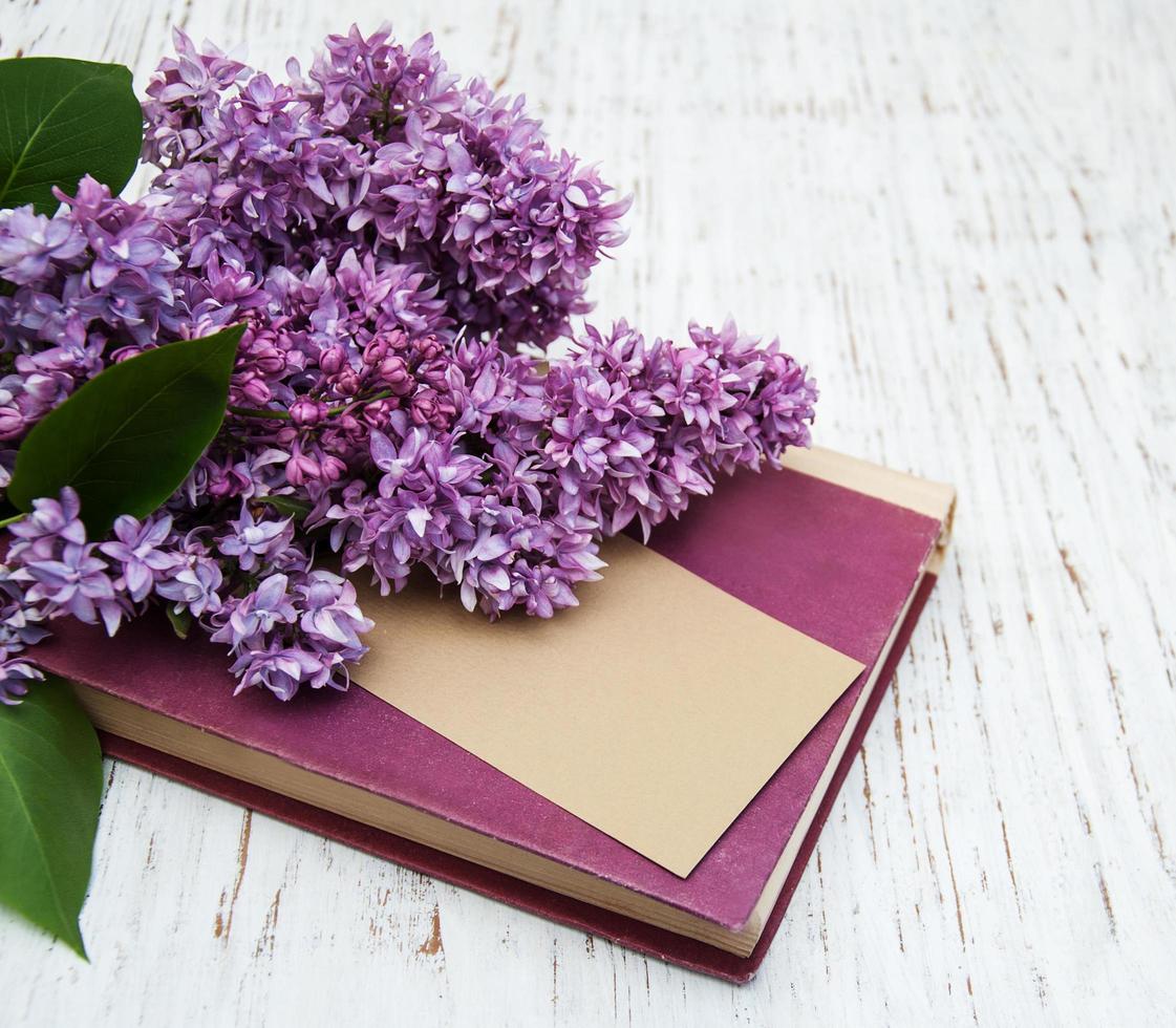 flores lilás e um livro antigo com um cartão em um fundo de madeira foto