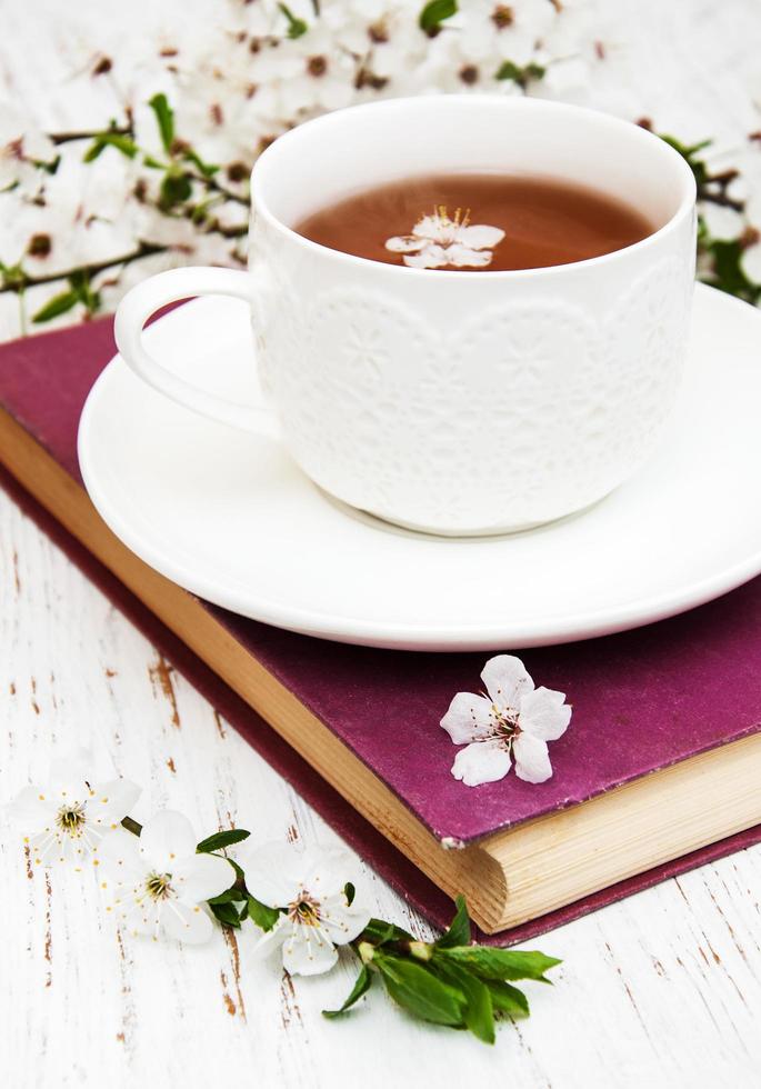 xícara de chá e flores de cerejeira com um livro antigo em um fundo de madeira foto