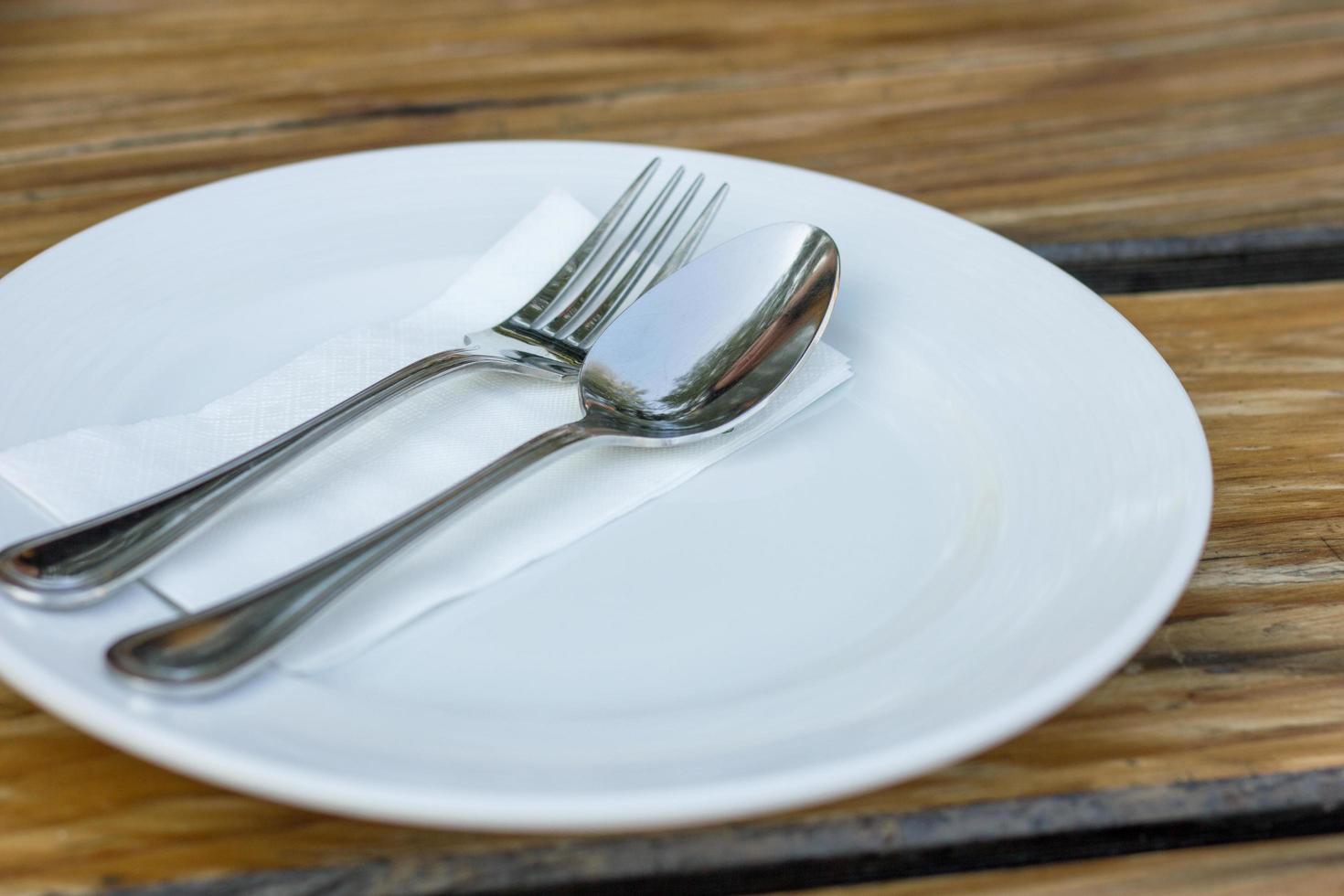 garfo e colher com prato branco na mesa de madeira foto