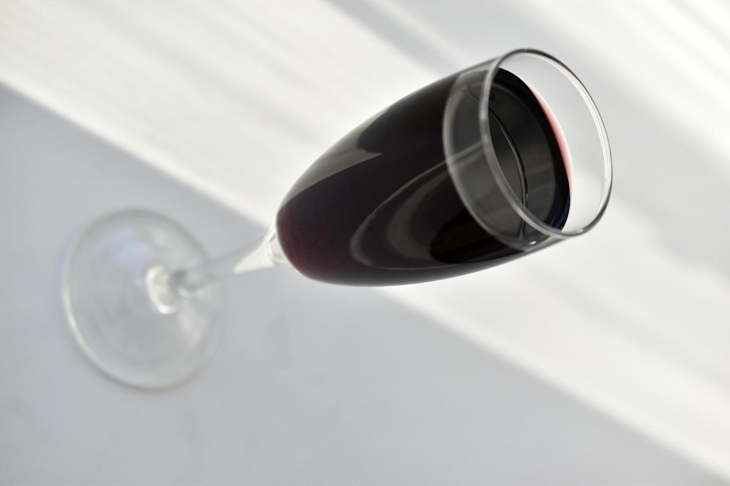 pequeno copo de vinho tinto em um fundo branco com sombras foto