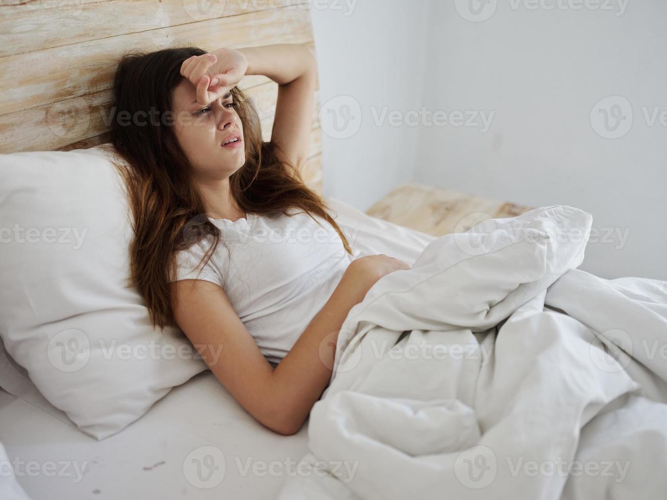 chateado mulher segurando mão em testa temperatura saúde problemas deitado dentro cama foto