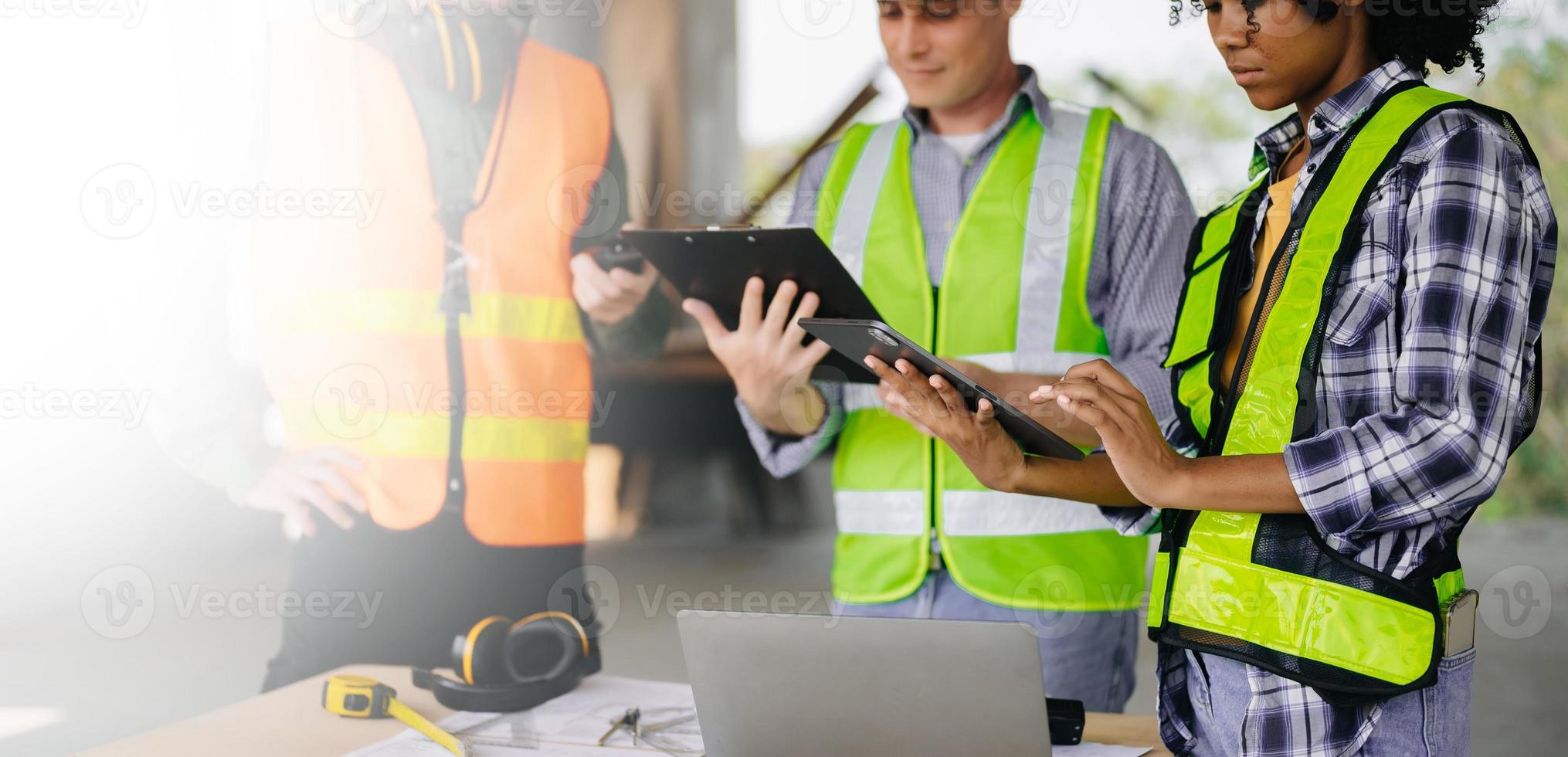 colegas discutindo trabalho de dados e tablet, laptop com no projeto arquitetônico no canteiro de obras na mesa no escritório foto