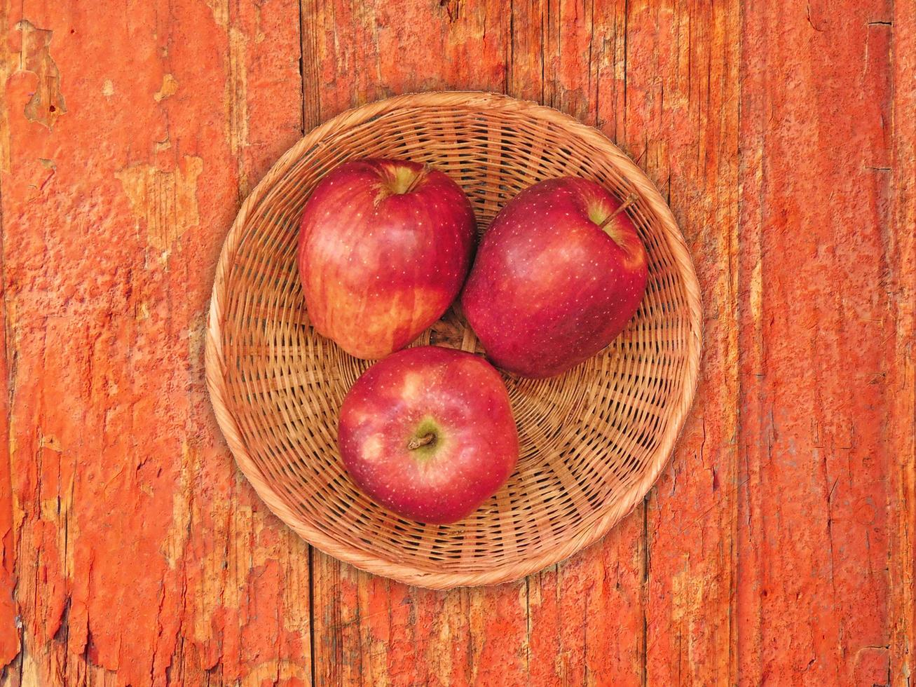 maçãs vermelhas em um prato de vime sobre um fundo de mesa de madeira foto