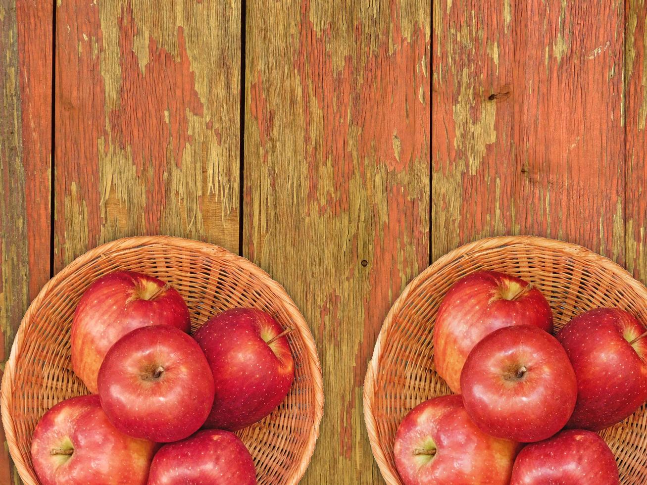maçãs vermelhas em um prato de vime sobre um fundo de mesa de madeira foto
