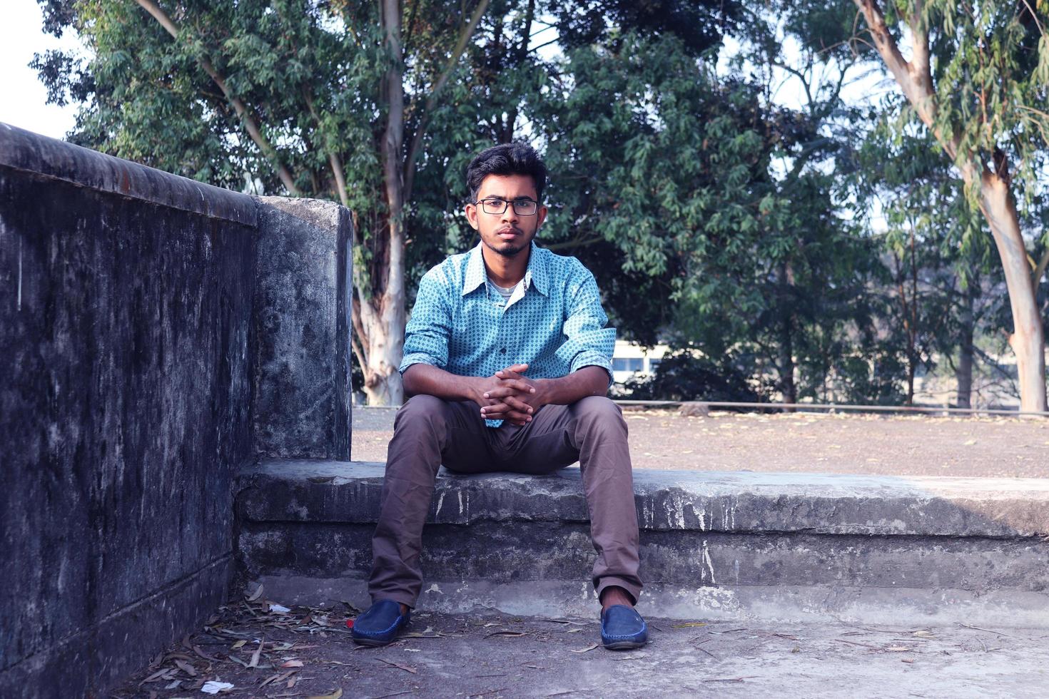 rangpur, Bangladesh 2023. depressivo adolescente homem sentado sozinho em parede dentro ao ar livre.desagradável dor. triste infeliz bonito homem. bangladeshi e Ásia Garoto sofrimento depressão. foto