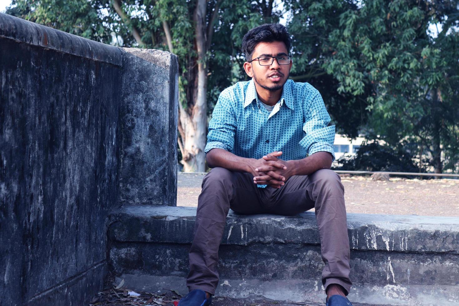 rangpur, Bangladesh 2023. depressivo adolescente homem sentado sozinho em parede dentro ao ar livre.desagradável dor. triste infeliz bonito homem. bangladeshi e Ásia Garoto sofrimento depressão. foto