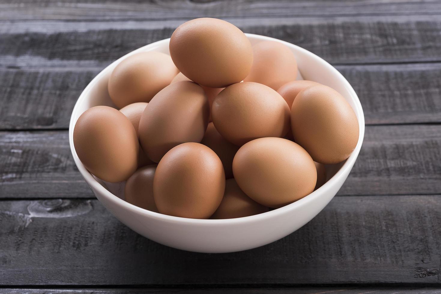 ovos de galinha frescos em uma tigela branca sobre uma mesa de madeira preta foto