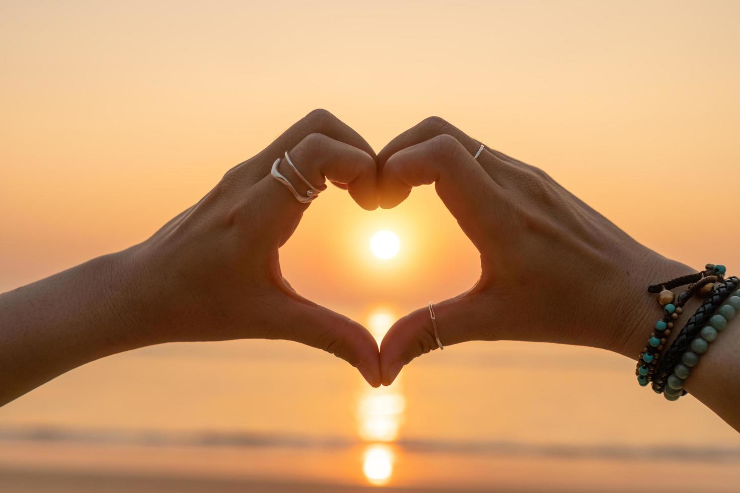 mãos de uma mulher fazendo um formato de coração em um céu do sol e fundo bokeh, conceito de amor dia dos namorados foto