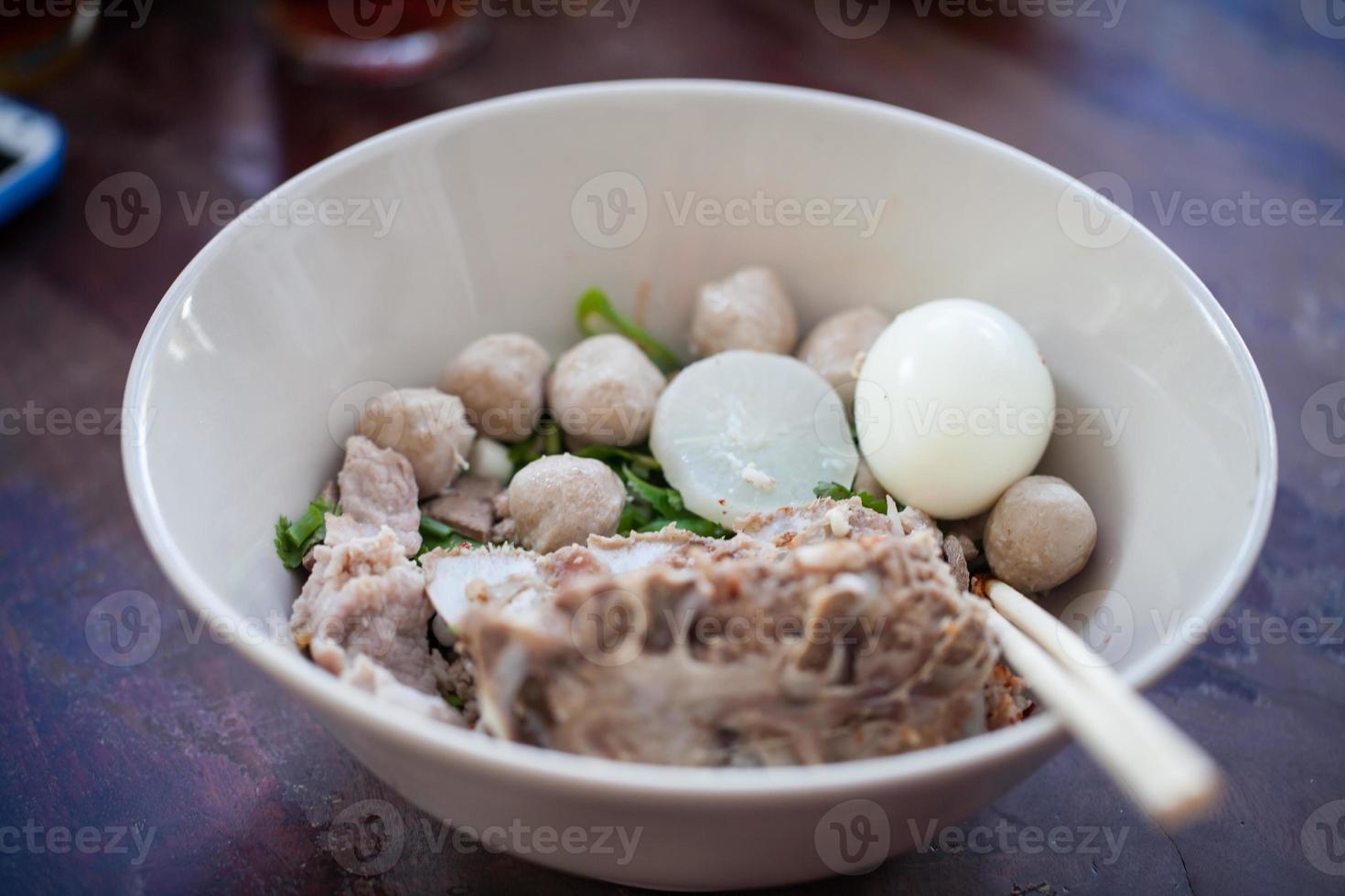 macarrão tailandês com carne de porco e almôndegas em prato branco foto