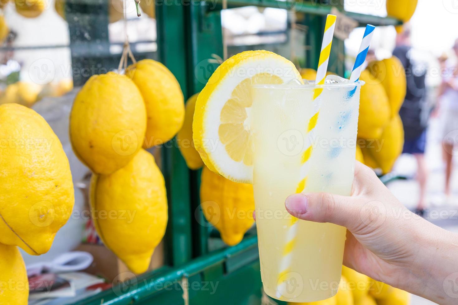 mão caucasiana com limonada fresca saudável durante o verão - fundo de limões foto