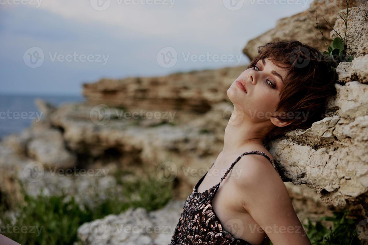 lindo mulher curto corte de cabelo posando sentado em a pedras elegância foto