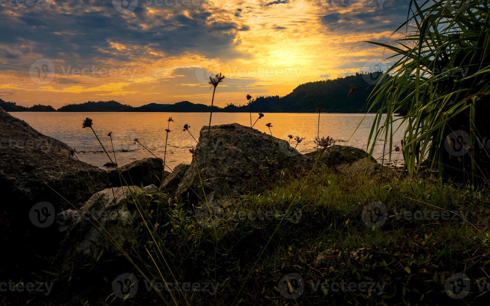 pôr do sol dentro uma de praia com pedras. silhueta do ilha dentro a fundo foto