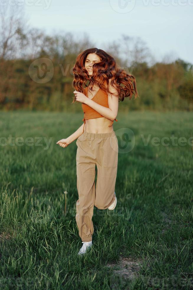 uma mulher trabalho Fora e corre através a campo dentro a parque com uma sorrir dentro uma Boa humor olhando às a lindo verão natureza por aí dela foto