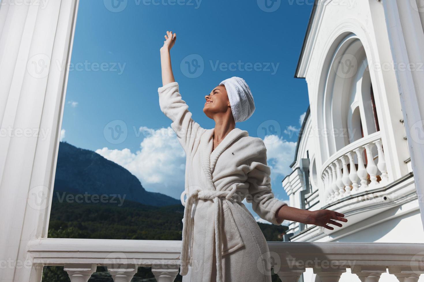 mulher dentro uma branco roupão com uma toalha em dela cabeça em a sacada do a hotel arquitetura foto