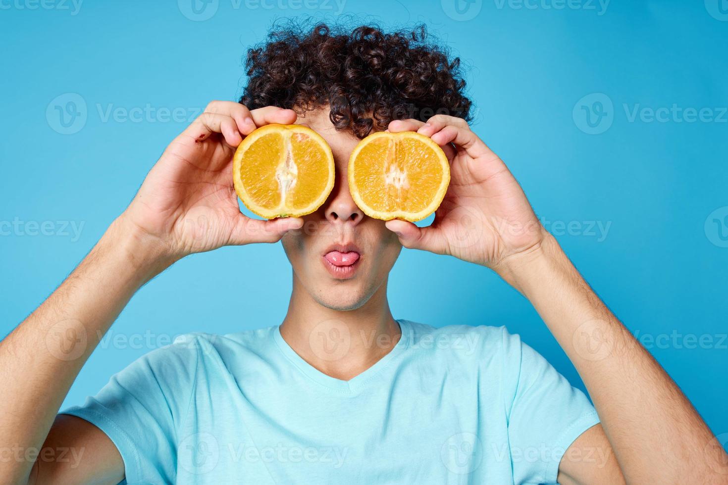 homem com encaracolado cabelo laranjas segurando fruta estúdio azul fundo foto