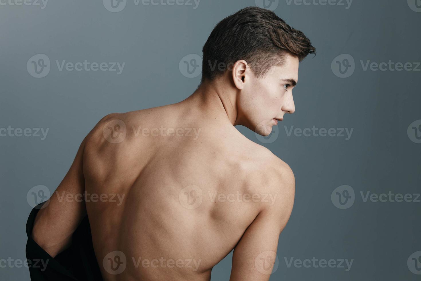 sexy homem com uma nu costas parece para a lado em uma cinzento fundo traseiro Visão do uma ginástica esporte foto