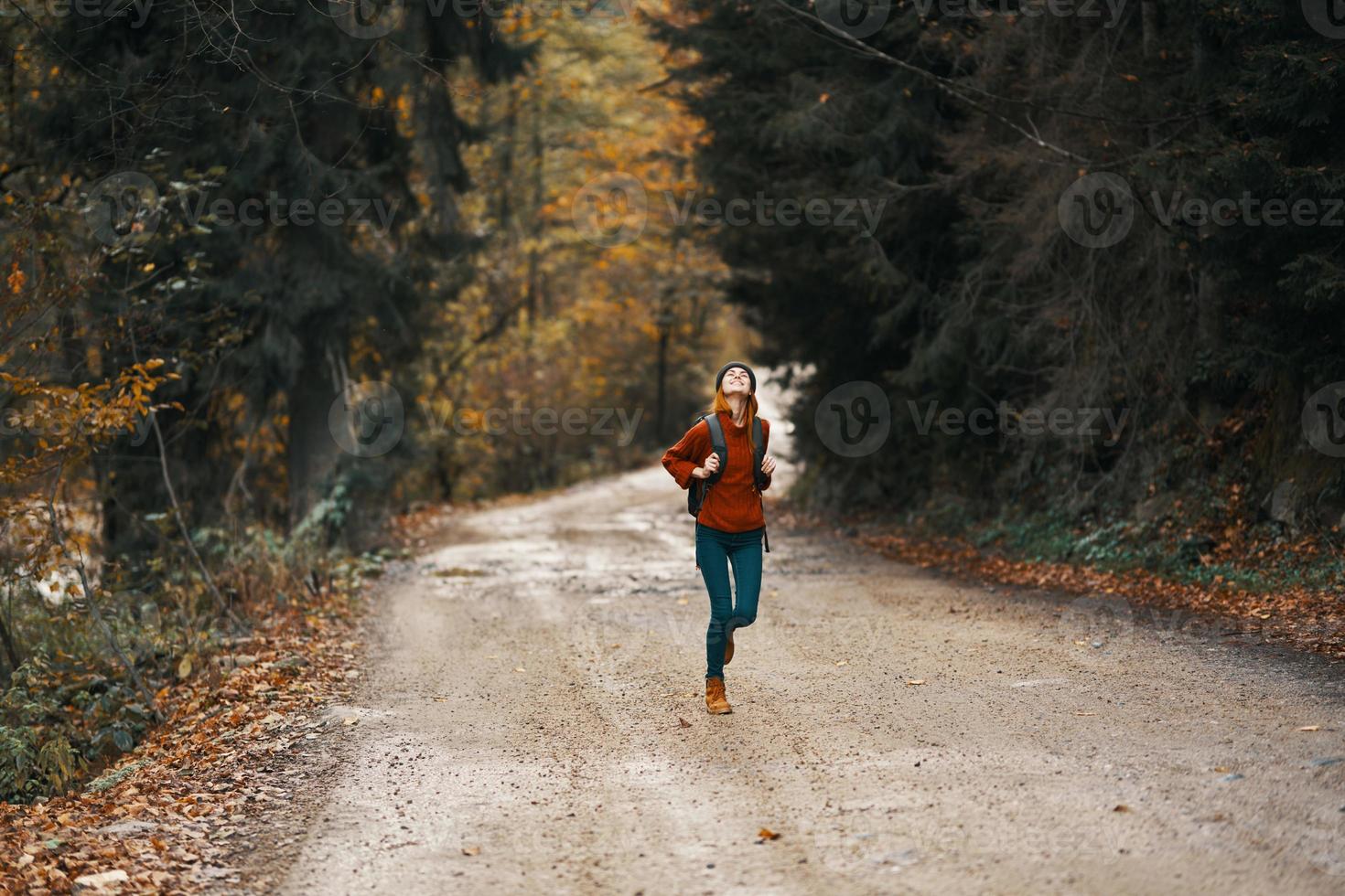 enérgico mulher corrida ao longo a estrada com mochila dentro outono floresta foto