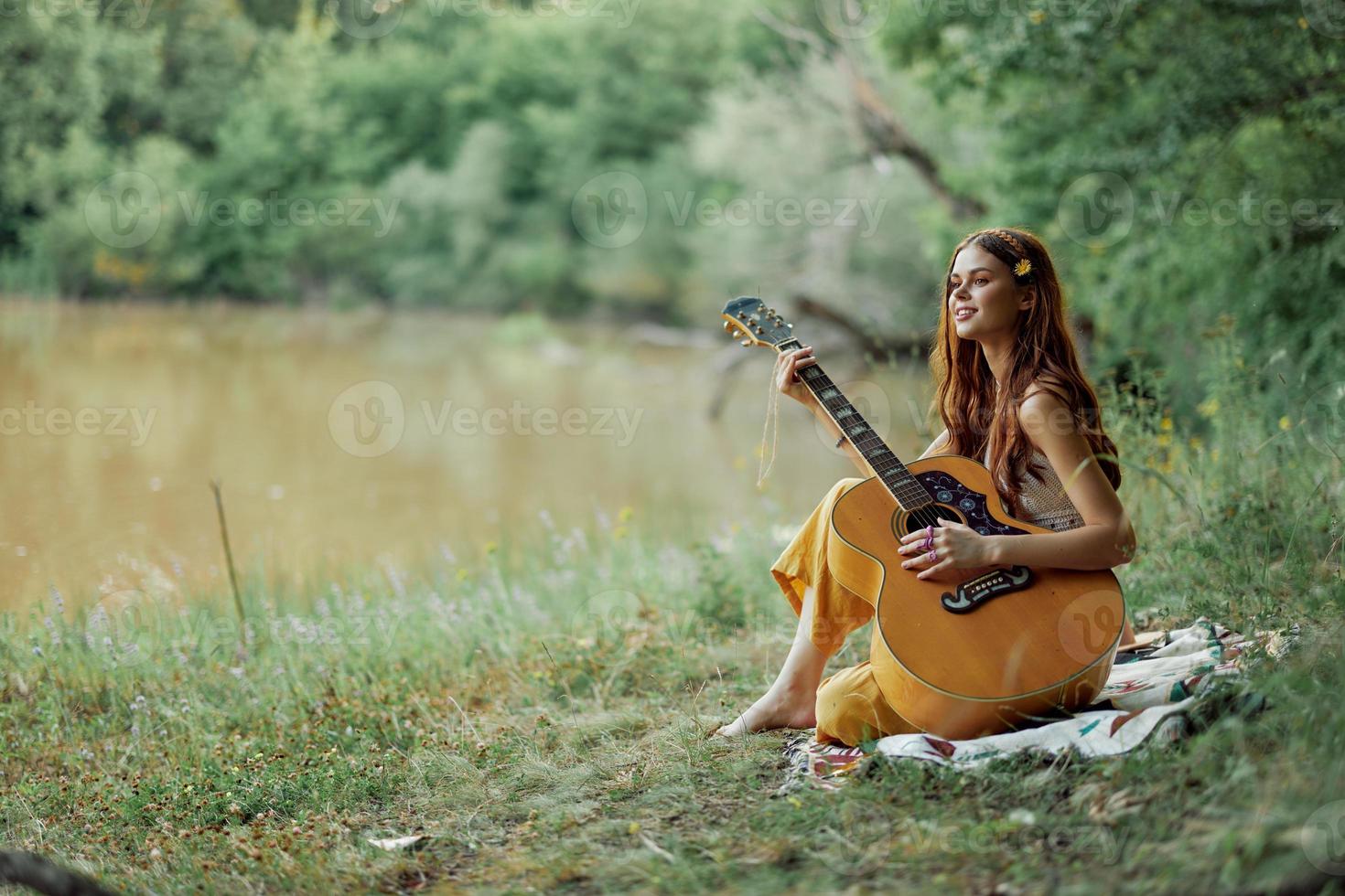 uma hippie mulher jogando dela guitarra sorrisos e canta canções dentro natureza sentado em uma xadrez dentro a tarde dentro a pôr do sol luz solar. uma estilo de vida dentro harmonia com a corpo e natureza foto