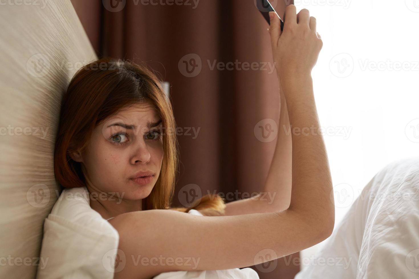 mulher com Móvel telefone levando As fotos do ela mesma deitado dentro cama debaixo a cobre