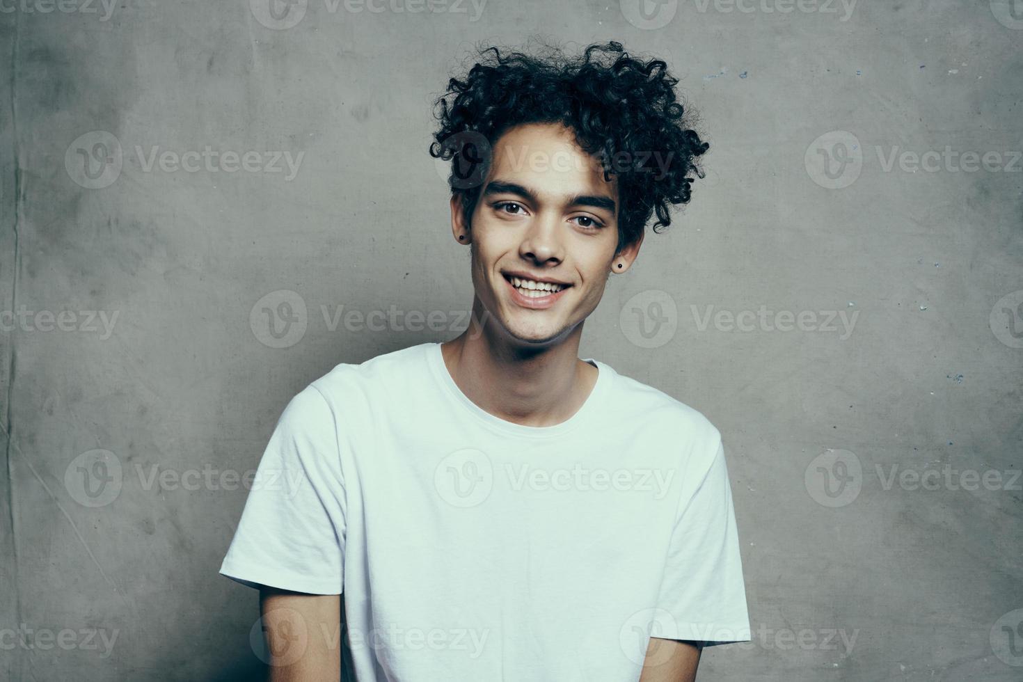 fofa cara com encaracolado cabelo dentro uma branco camiseta senta em cadeiras estúdio moda foto