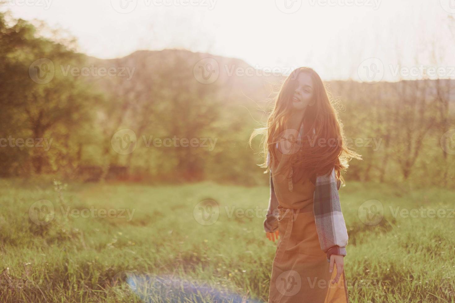 uma mulher corrida através uma campo em uma verão dia com grandes fluindo cabelo dentro a raios do a configuração Sol. a conceito do liberdade e harmonia com natureza foto