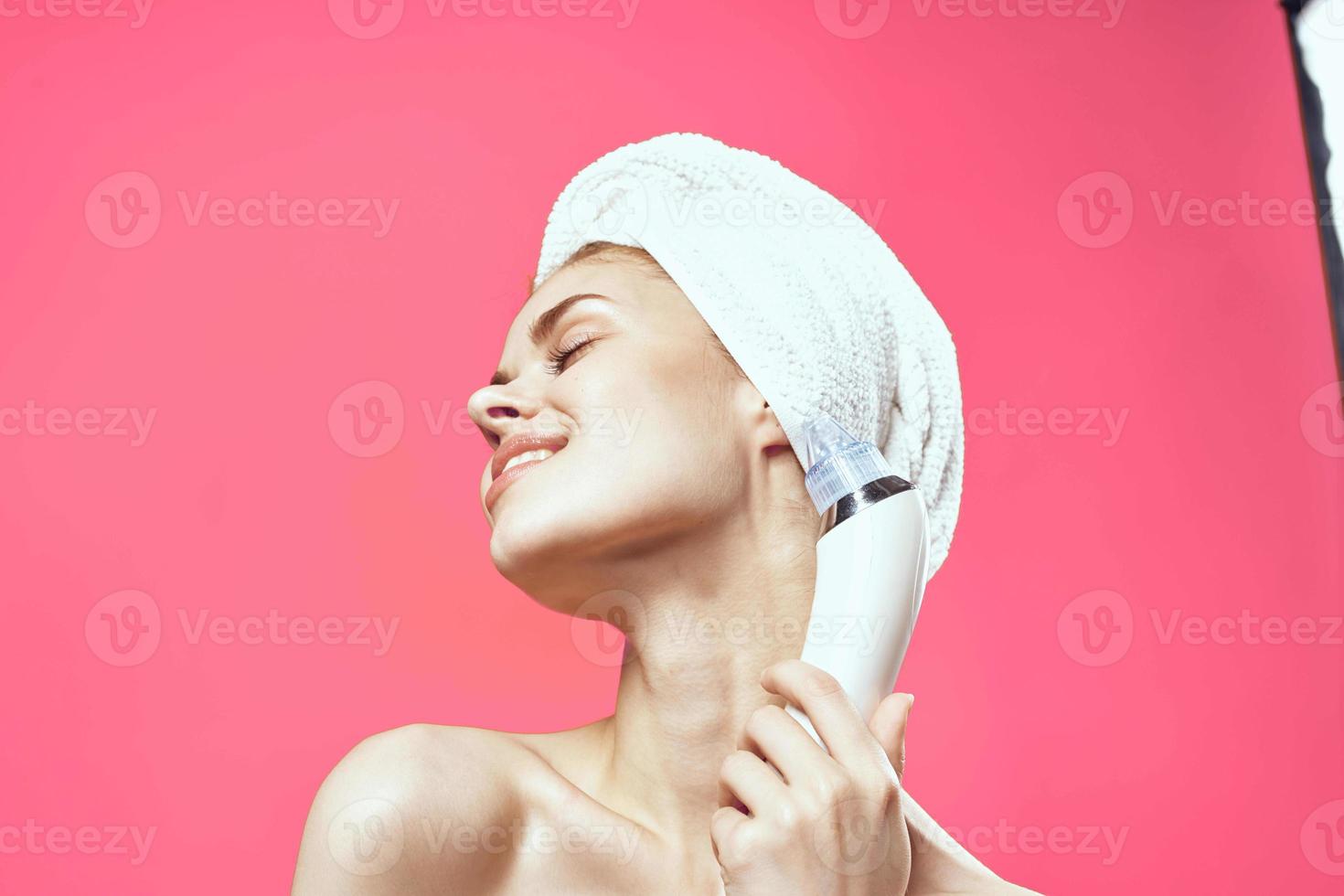 alegre mulher com uma toalha em dela cabeça vácuo face limpeza Rosa fundo foto