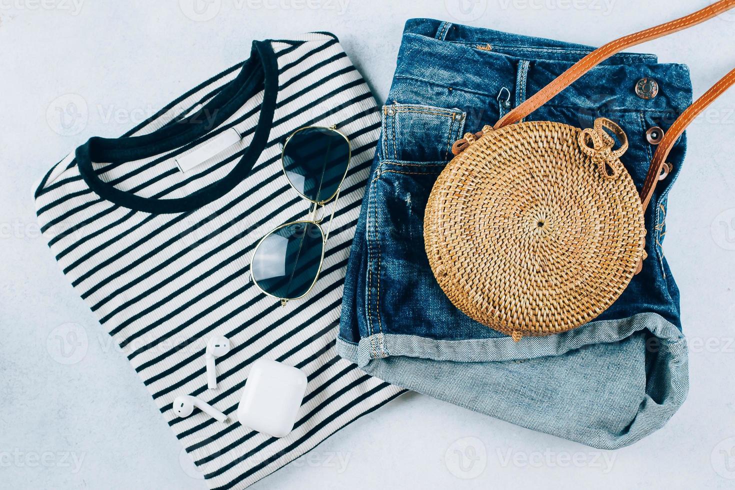 Primavera e verão mulheres roupas e acessórios. listrado camiseta, azul jeans calção e elegante orgânico rattan bolsa. plano deitar foto, topo Visão foto