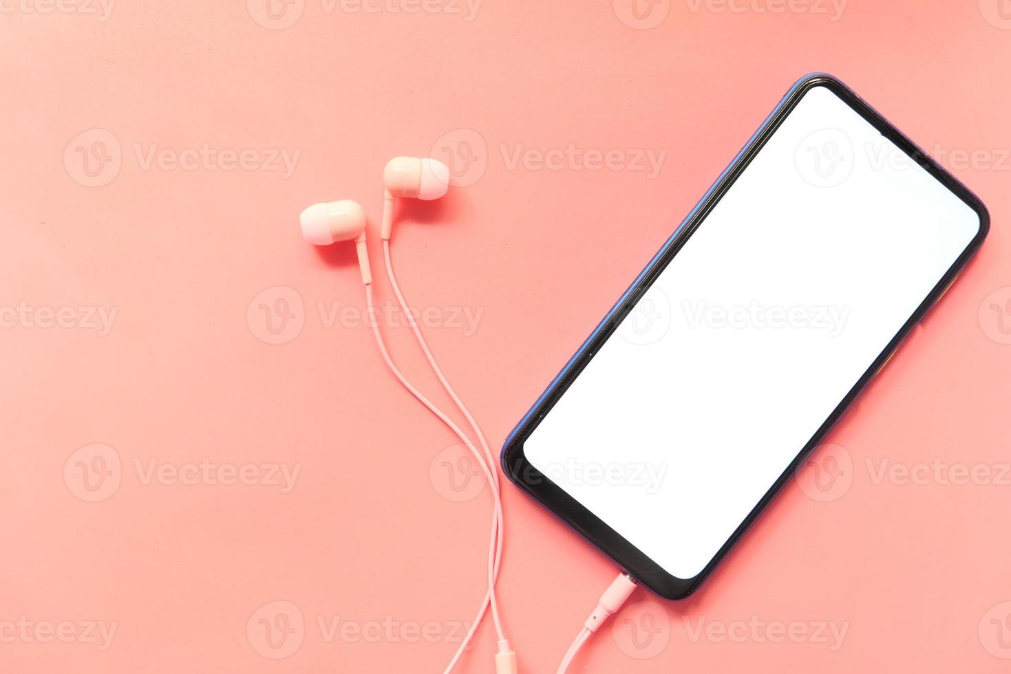 telefone inteligente com tela vazia e fones de ouvido em fundo rosa foto