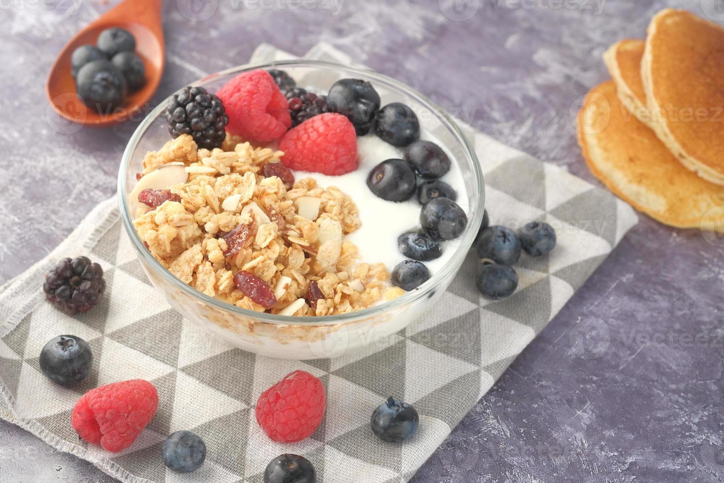 granola com iogurte e frutas vermelhas em uma tigela em fundo neutro foto