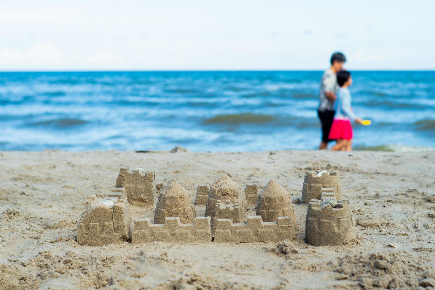 o castelo de areia construído pelo molde com pessoas desfocadas caminhando na praia ao fundo foto