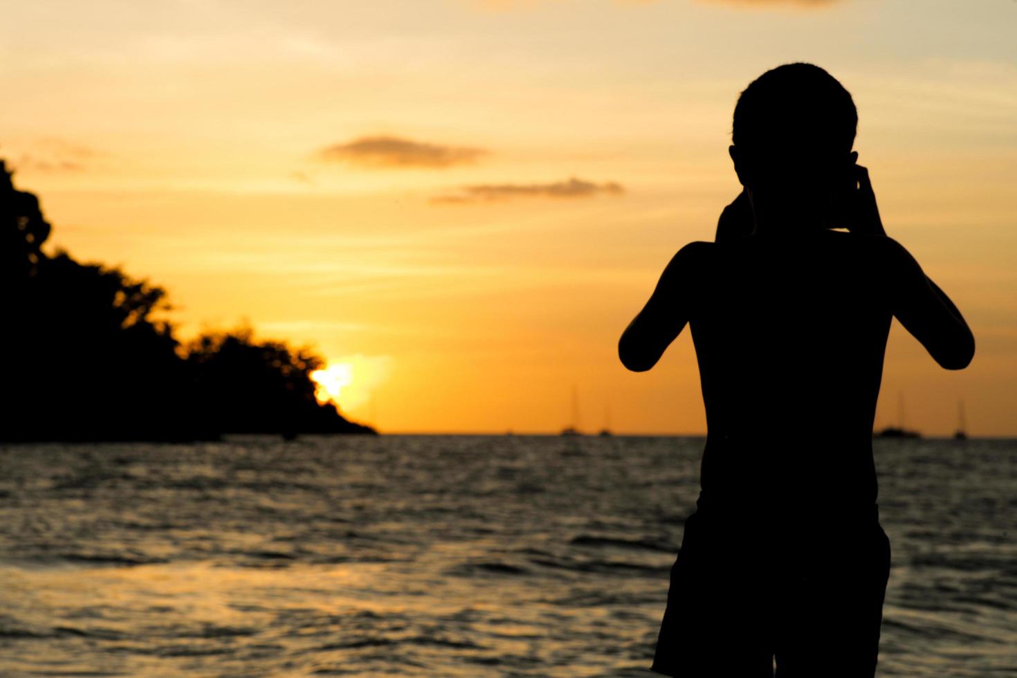 retrato da silhueta de um menino tirando uma cena de paisagem marinha na praia com a luz do pôr do sol foto