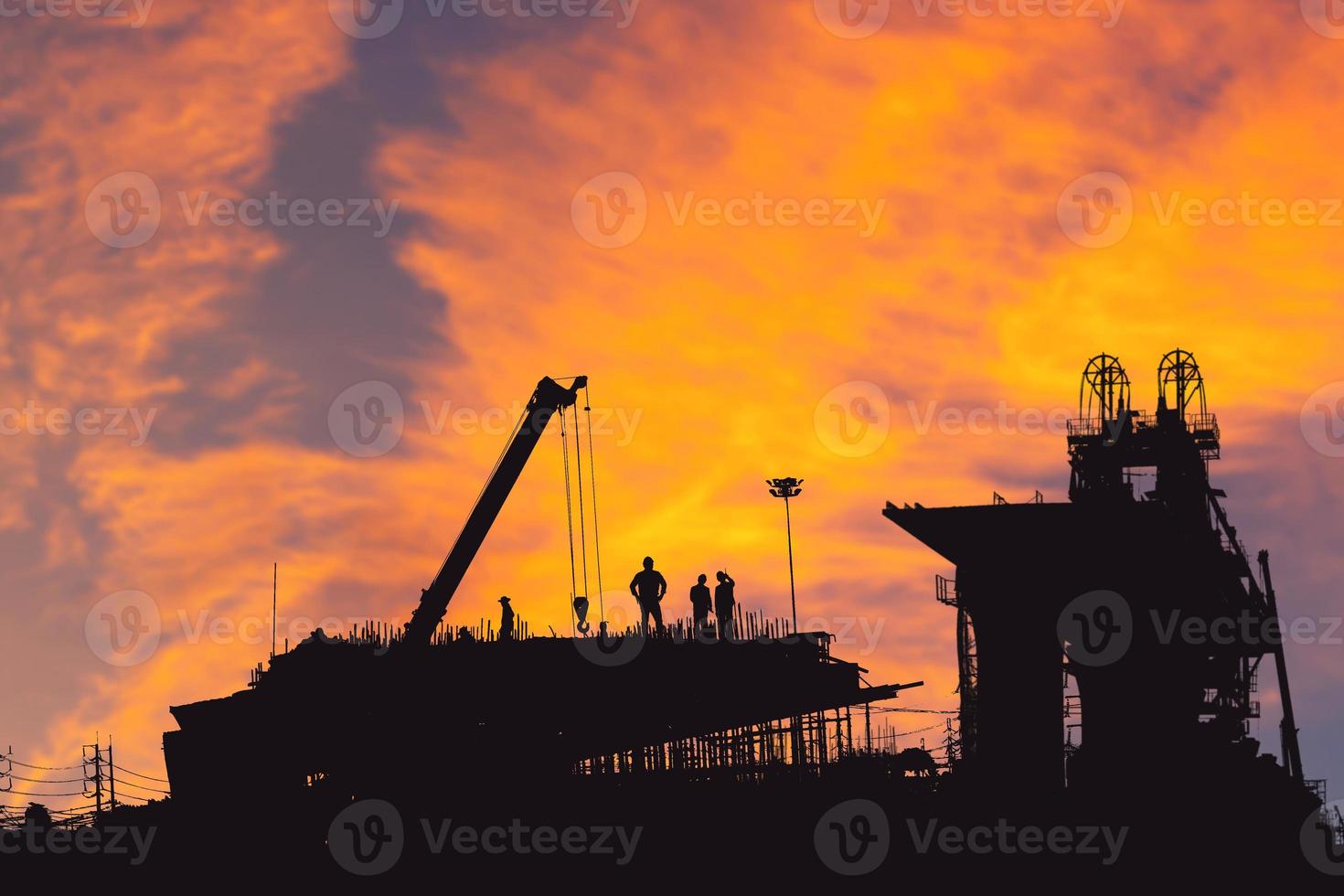 silhueta de engenheiro e trabalhador verificando projeto no fundo do canteiro de obras, canteiro de obras ao pôr do sol na noite foto