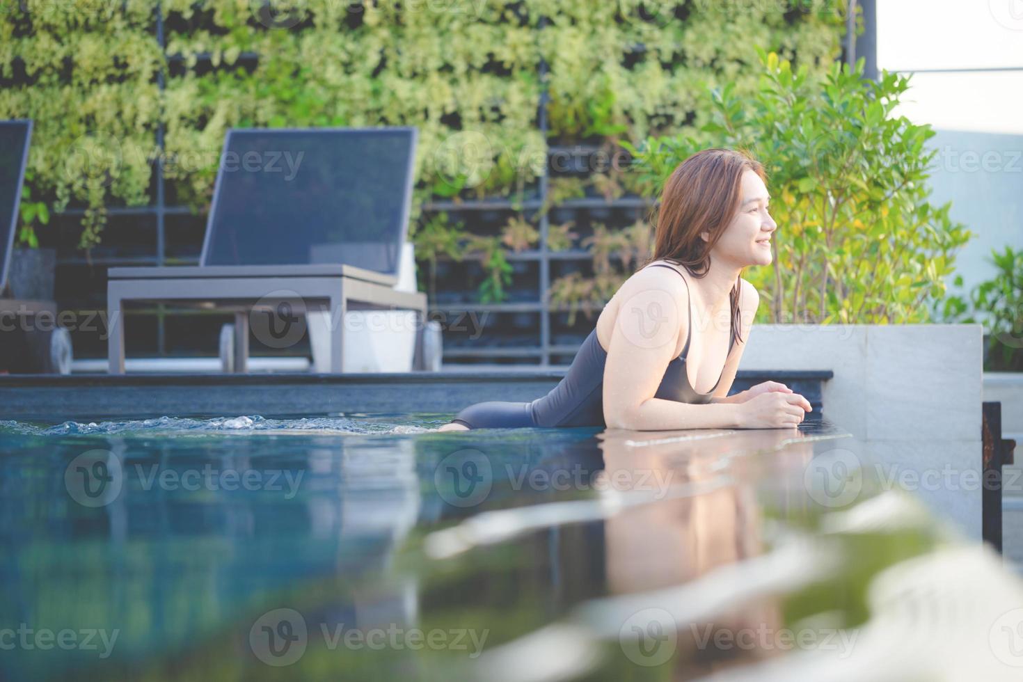 ásia mulher relaxar dentro natação piscina em cobertura topo com pôr do sol Visão com Alto subir skyscape urbano centro da cidade, felicidade estilo de vida e feriados conceitos foto