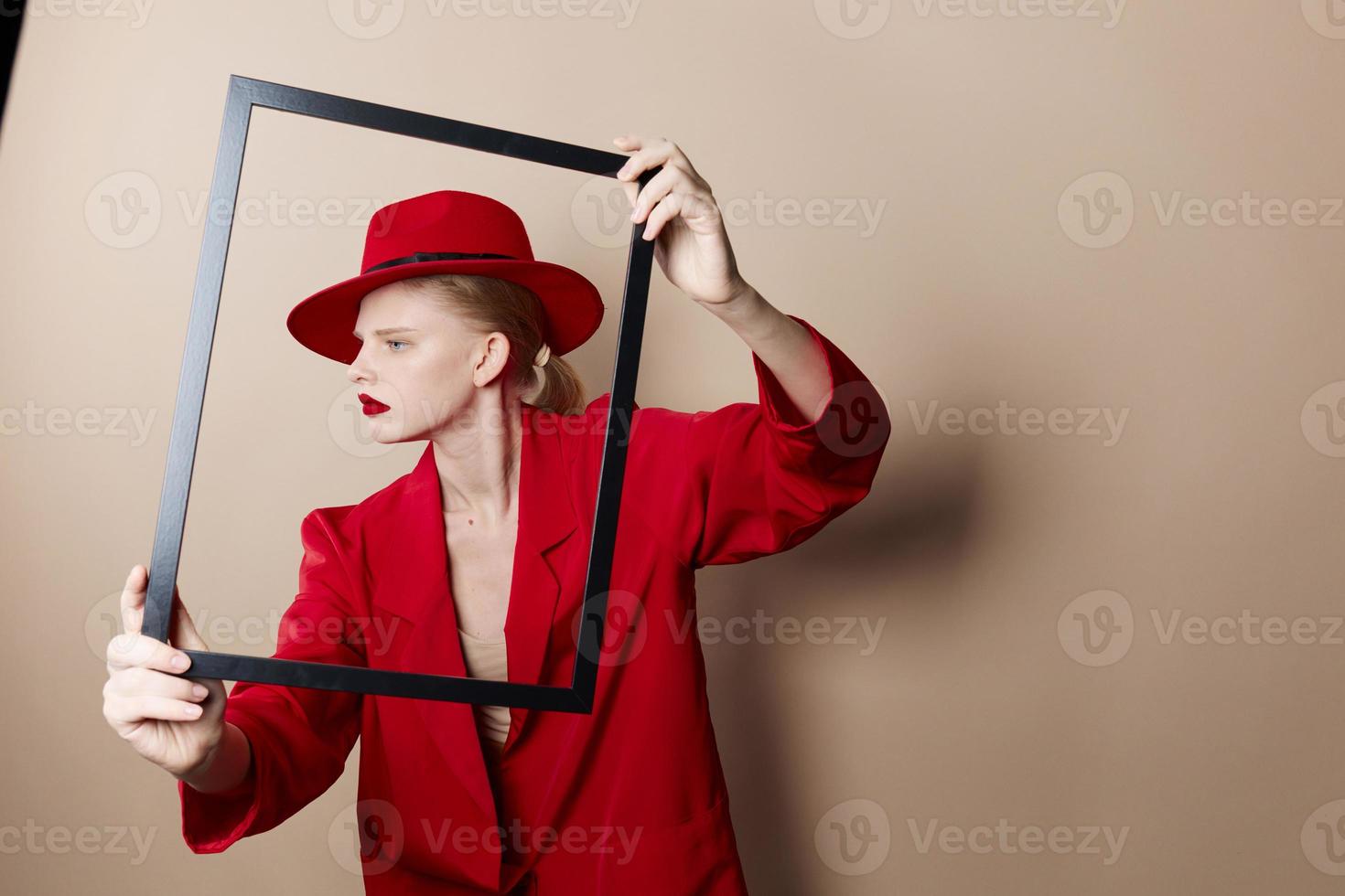 glamouroso mulher quadro, Armação dentro mão dentro vermelho chapéu e Jaqueta estilo de vida posando foto