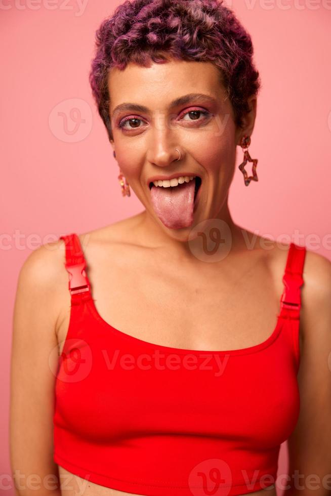 moda retrato do uma mulher com uma curto corte de cabelo do roxa cor e uma sorrir com dentes dentro uma vermelho topo em uma Rosa fundo felicidade foto