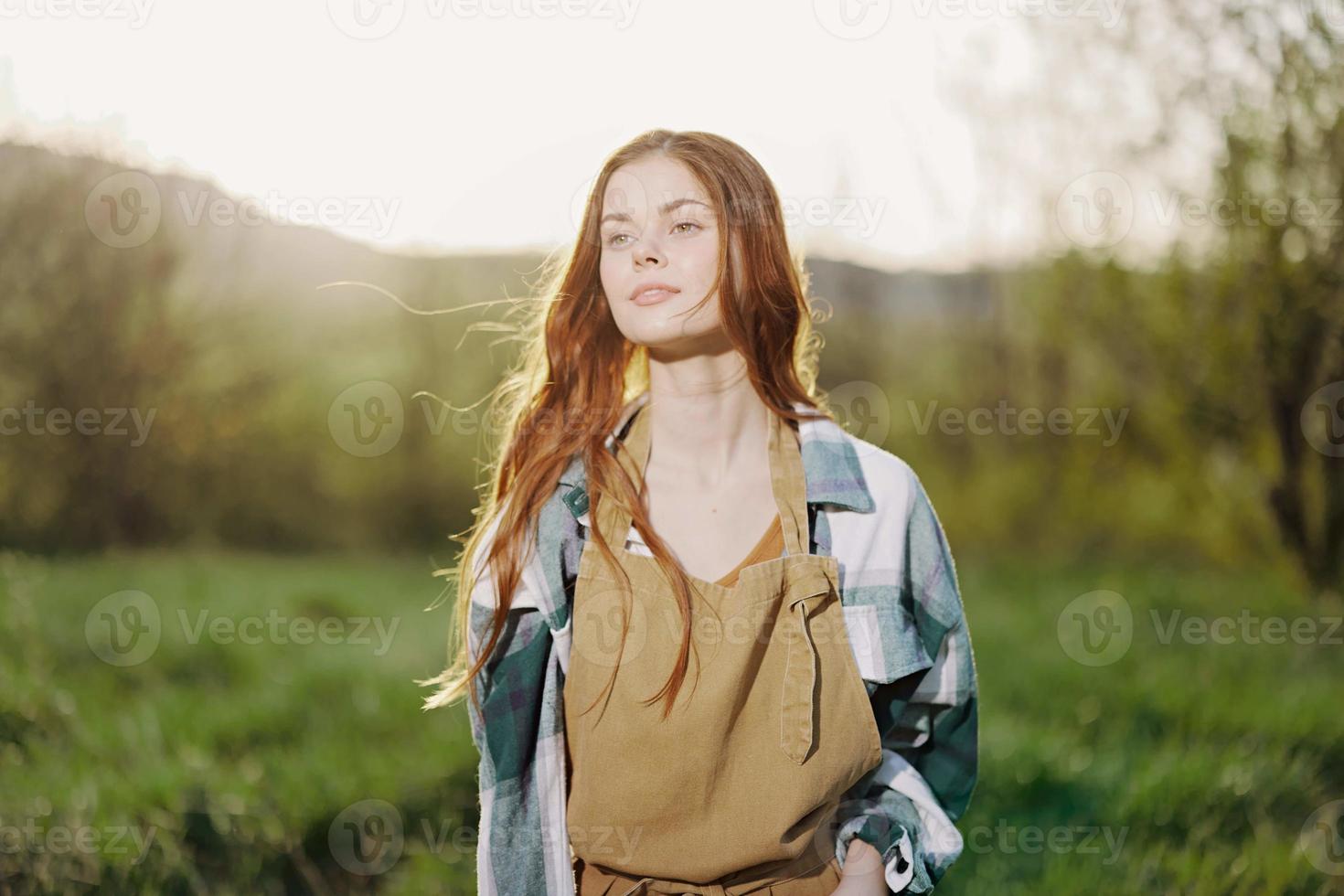 retrato do uma jovem sorridente mulher dentro trabalhos roupas xadrez camisa e avental dentro natureza dentro a tarde depois de trabalhos foto