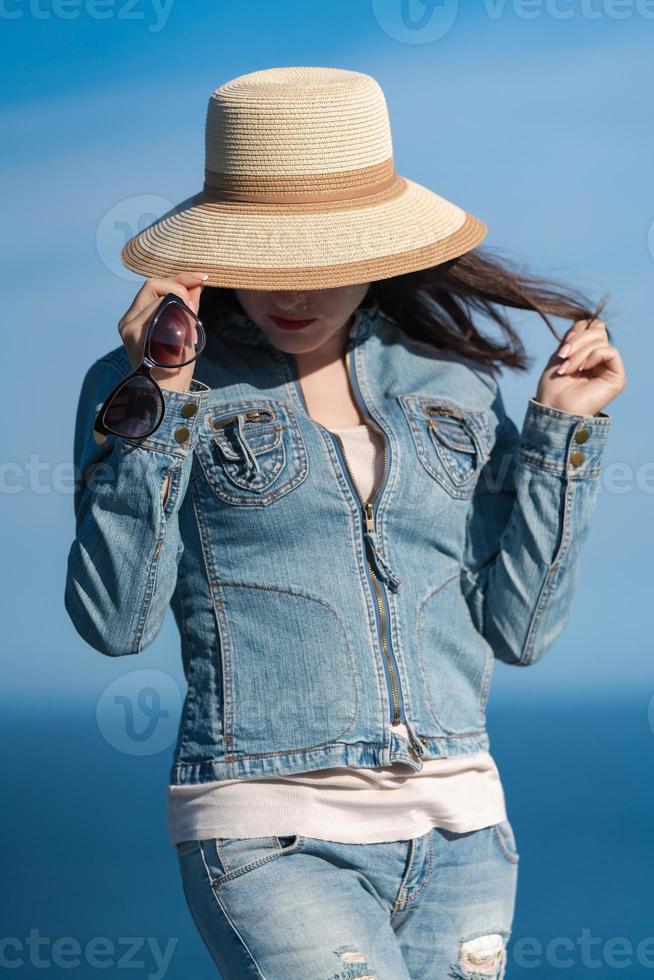 retrato do fêmea dentro jeans Jaqueta e jeans se escondendo com Palha chapéu sobre dele face foto