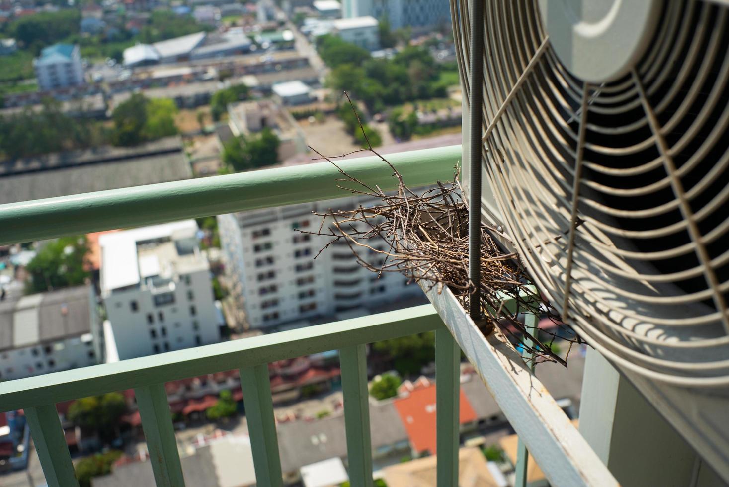 vista de cima do ninho de pássaro na gaiola de aço do ar-condicionado no terraço do condomínio alto com fundo desfocado da cidade na manhã de sol foto