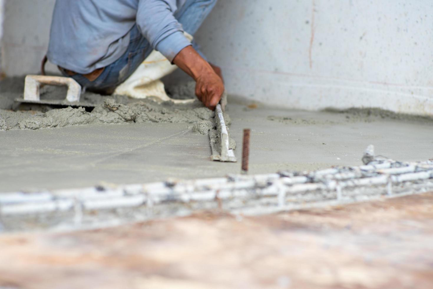 foco seletivo nas mãos dos trabalhadores usando a espátula de madeira nivelando a superfície do piso de cimento foto