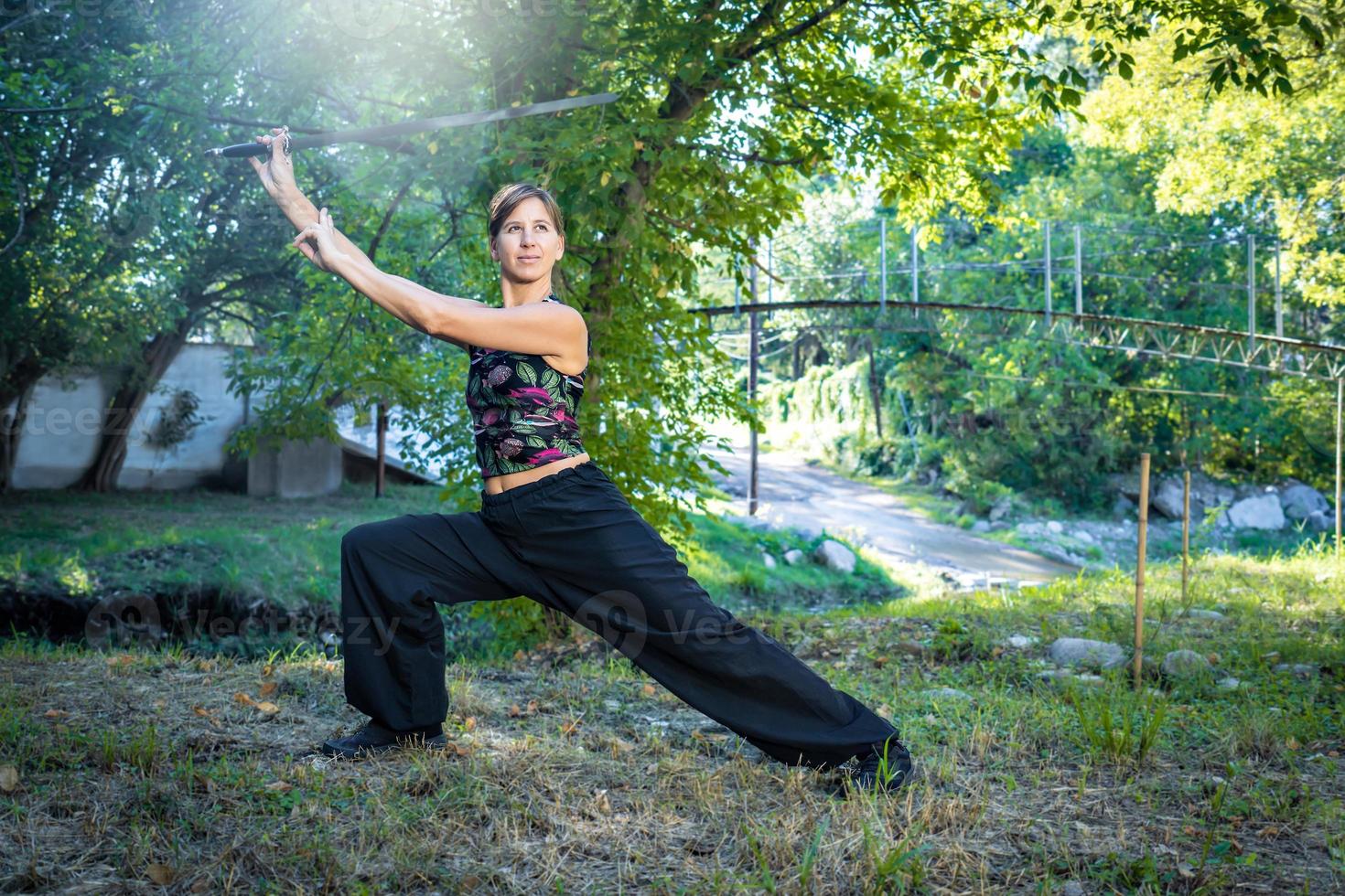 mulher é praticando a chinês marcial arte do tai chi com dela espada de a rio. foto