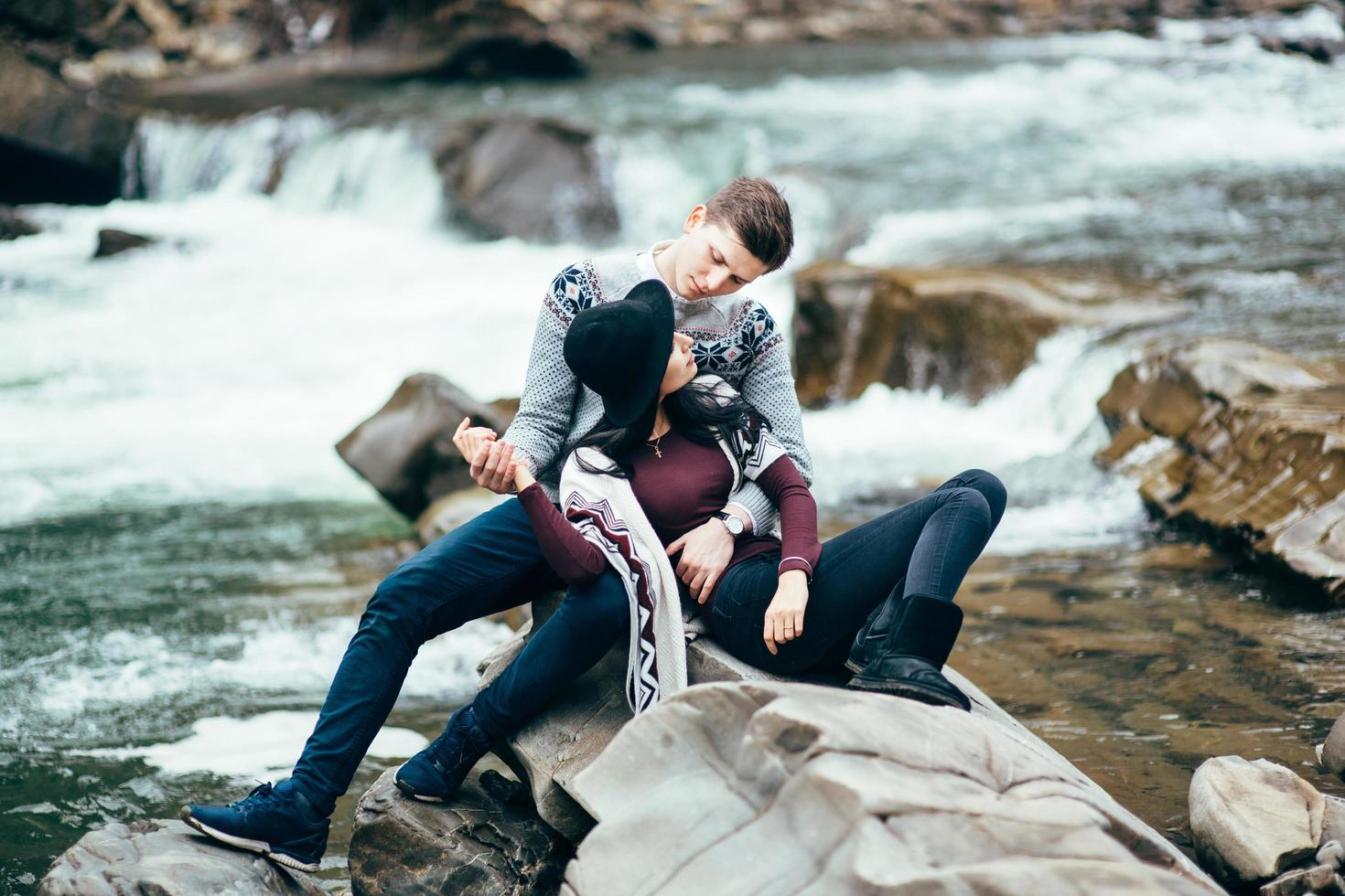 rapaz e moça em suéteres quentes caminhando ao longo de um rio na montanha, história de amor foto