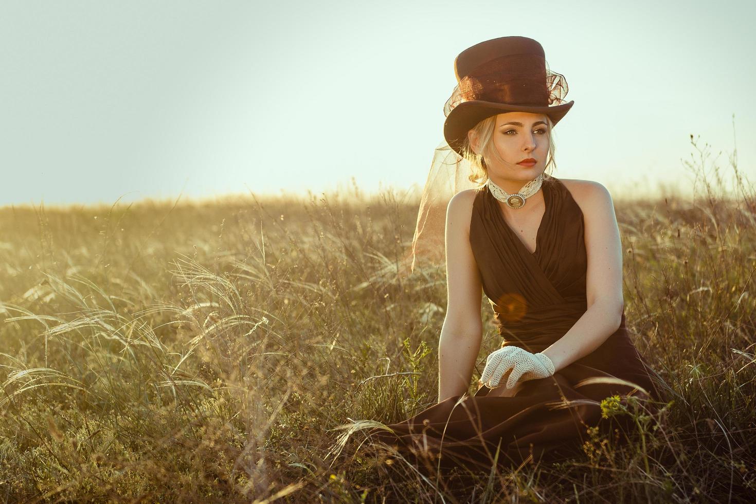 jovem loira em um vestido vintage marrom e cartola na grama foto