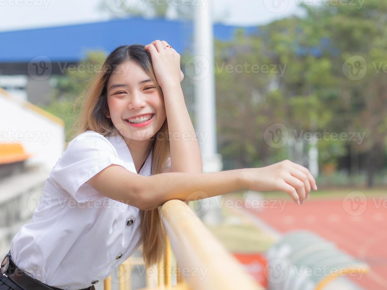 ásia lindo jovem mulher aluna é sorridente e olhando às Câmera em pé para presente alguma coisa com confiança dentro tailandês universidade fundo foto
