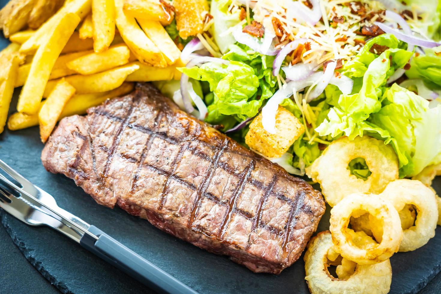 Bife de carne grelhada com batata frita anel de cebola com molho e vegetais frescos foto