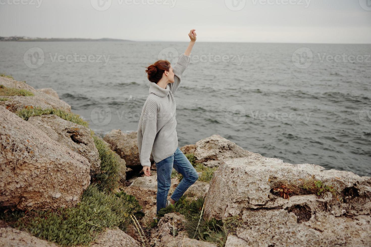 mulher dentro uma cinzento suéter carrinhos em uma rochoso costa natureza inalterado foto