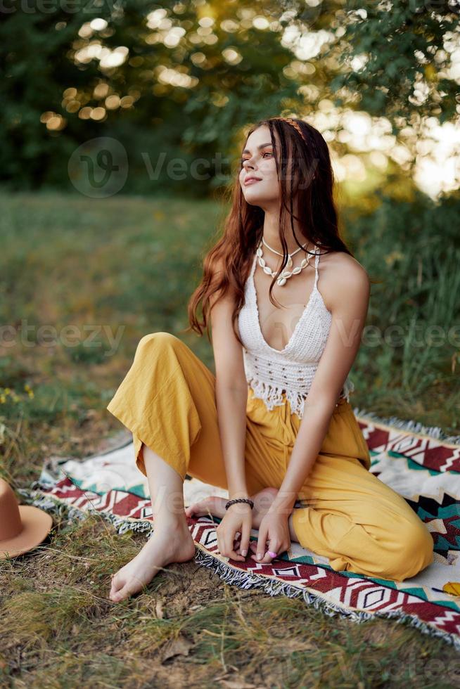 jovem lindo hippie mulher sentado em a terra dentro natureza dentro a outono dentro eco roupas dentro a pôr do sol luz, uma estilo de vida do viagem e harmonia com a mundo foto