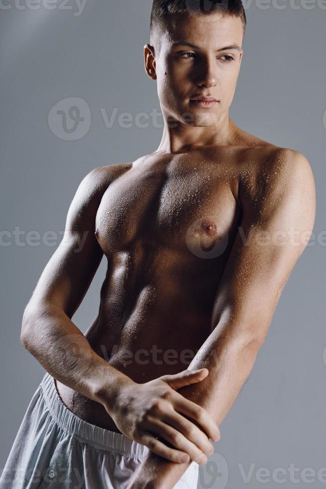 homem com uma bombeado tronco em uma cinzento fundo posando bíceps fisiculturista foto