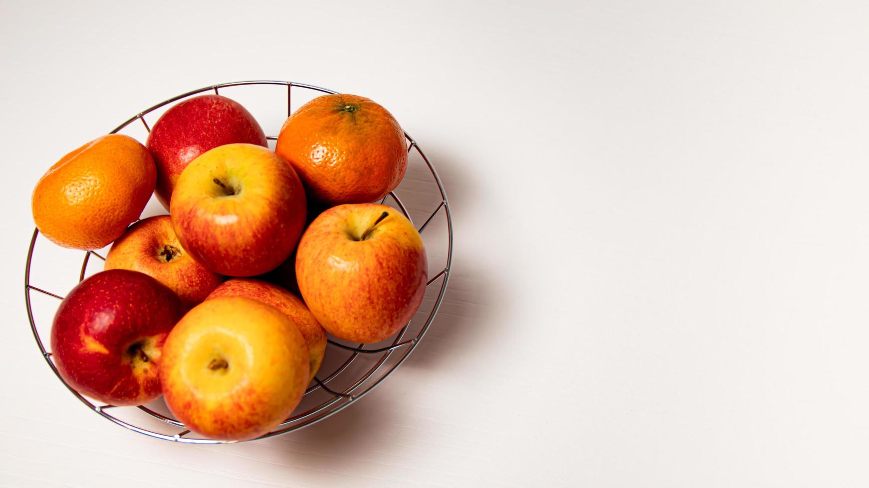 maduro maçãs e tangerinas dentro uma metal cesta em uma branco fundo foto